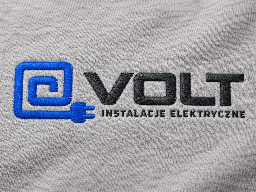 Zbliżenie dwukolorowego haftu logo na szarej bluzie — logo VOLT instalacje elektryczne