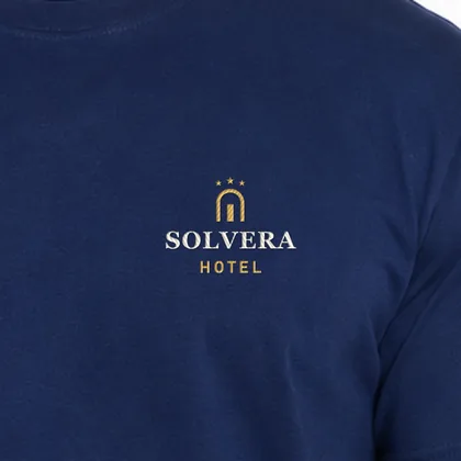 Zbliżenie haftu przykładowego logo hotelu SOLVERA na granatowej koszulce — złota i kremowa nić (logo wymyślone, zdjęcie poglądowe)